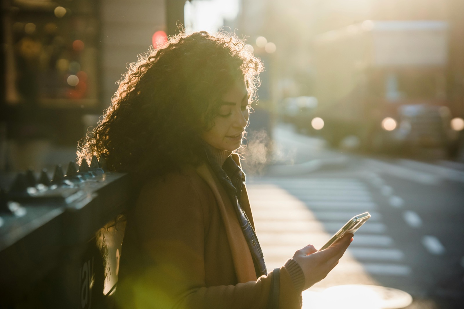 Woman checking her phone in warm evening light on a city street.